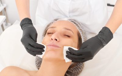 Cosmetologist removing facial cream mask from woman face skin with cosmetic wipes, rejuvenation skincare cosmetic procedure in beauty spa salon. Beautician hands holds napkins for remove face mask