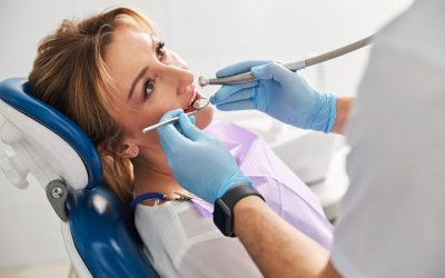 Medical person looking in a dental mirror at teeth reflection and applying a drill to this area